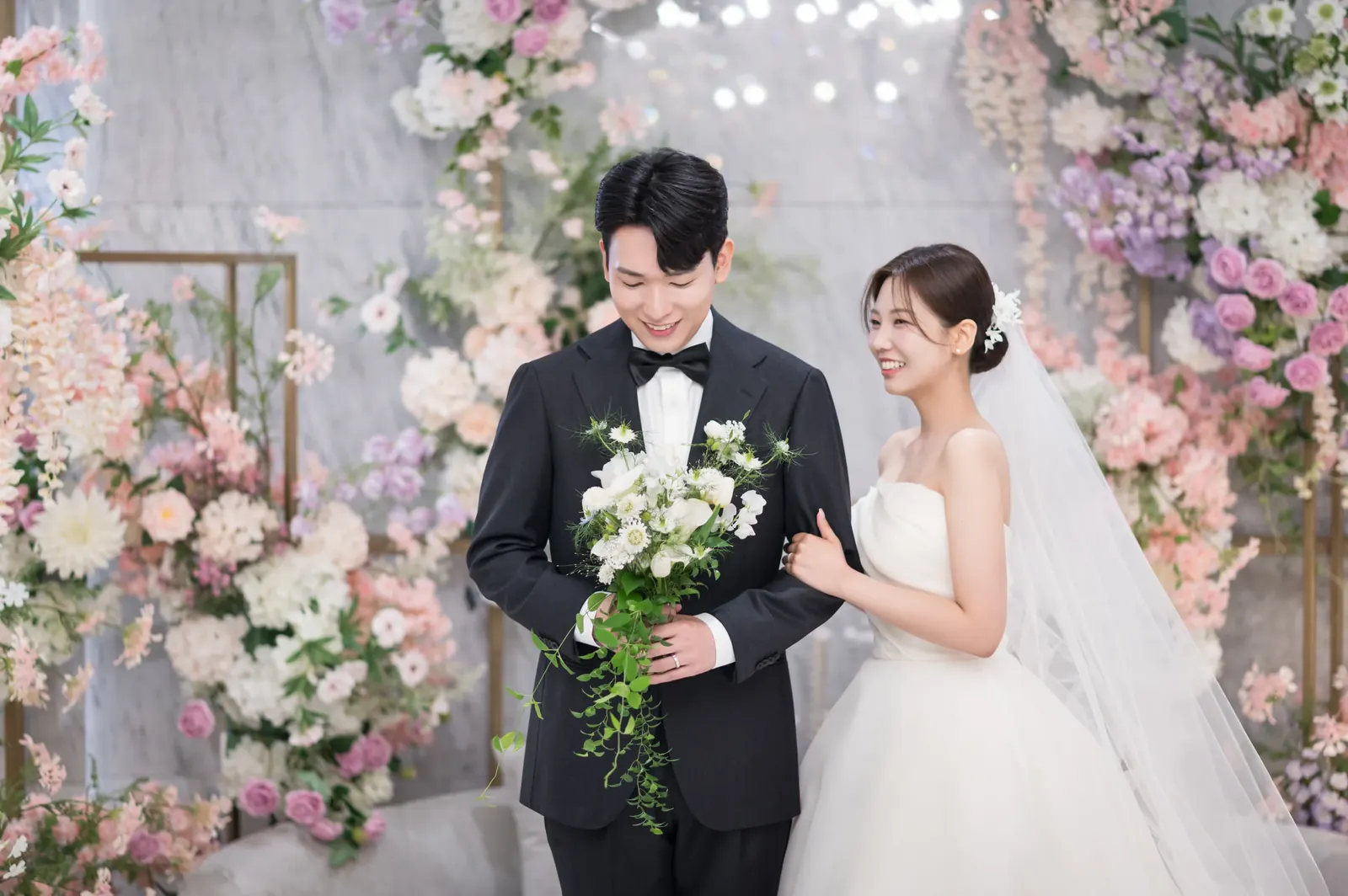 서울 본식스냅, 파스텔 꽃장식 앞에 나란히 선 신랑신부
